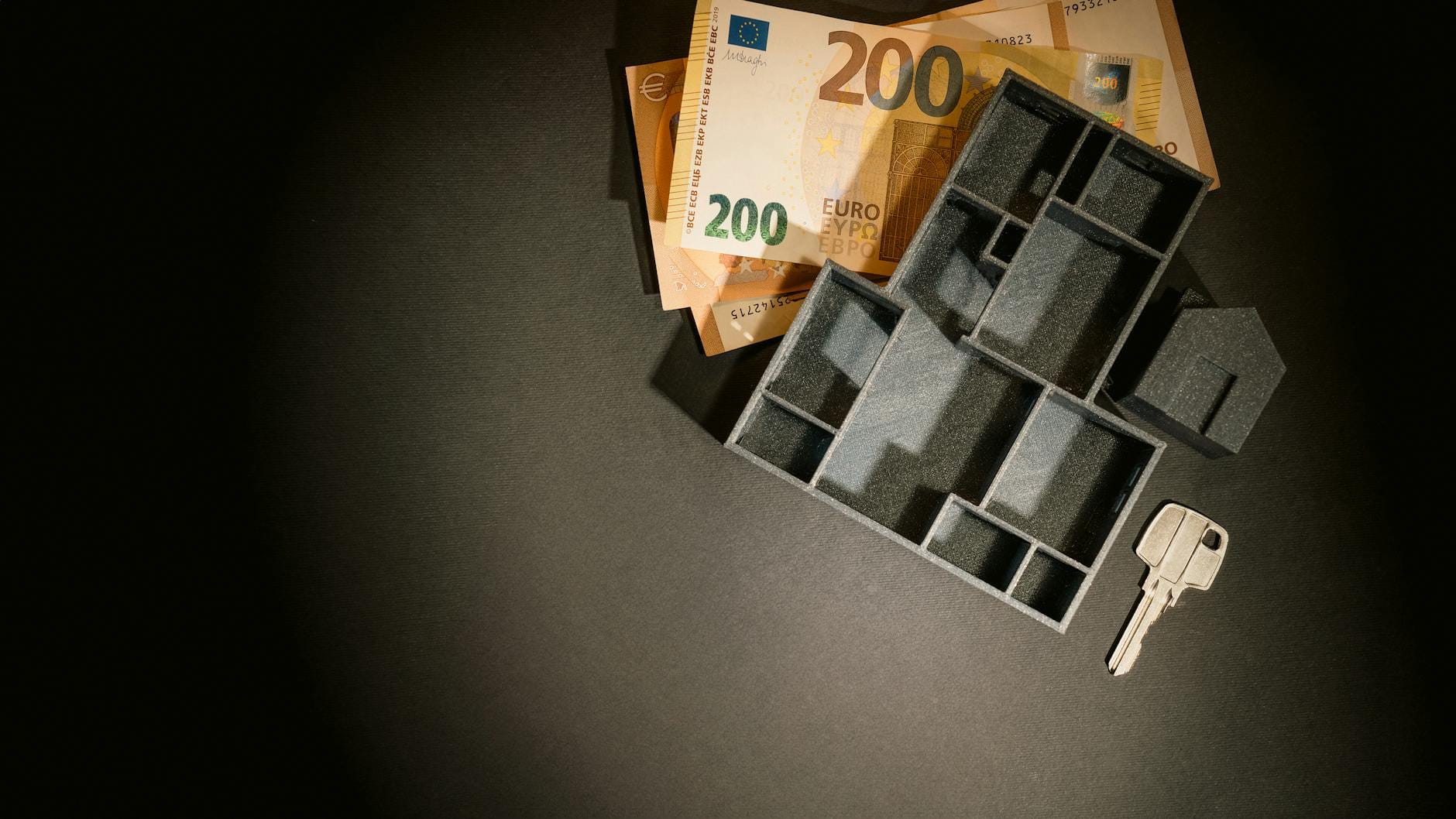 Banknoty euro, miniaturowy model budynku i klucz na stole