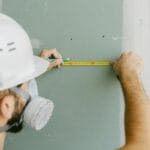 Pracownik budowlany mierzący płytę gk z użyciem narzędzi ręcznych