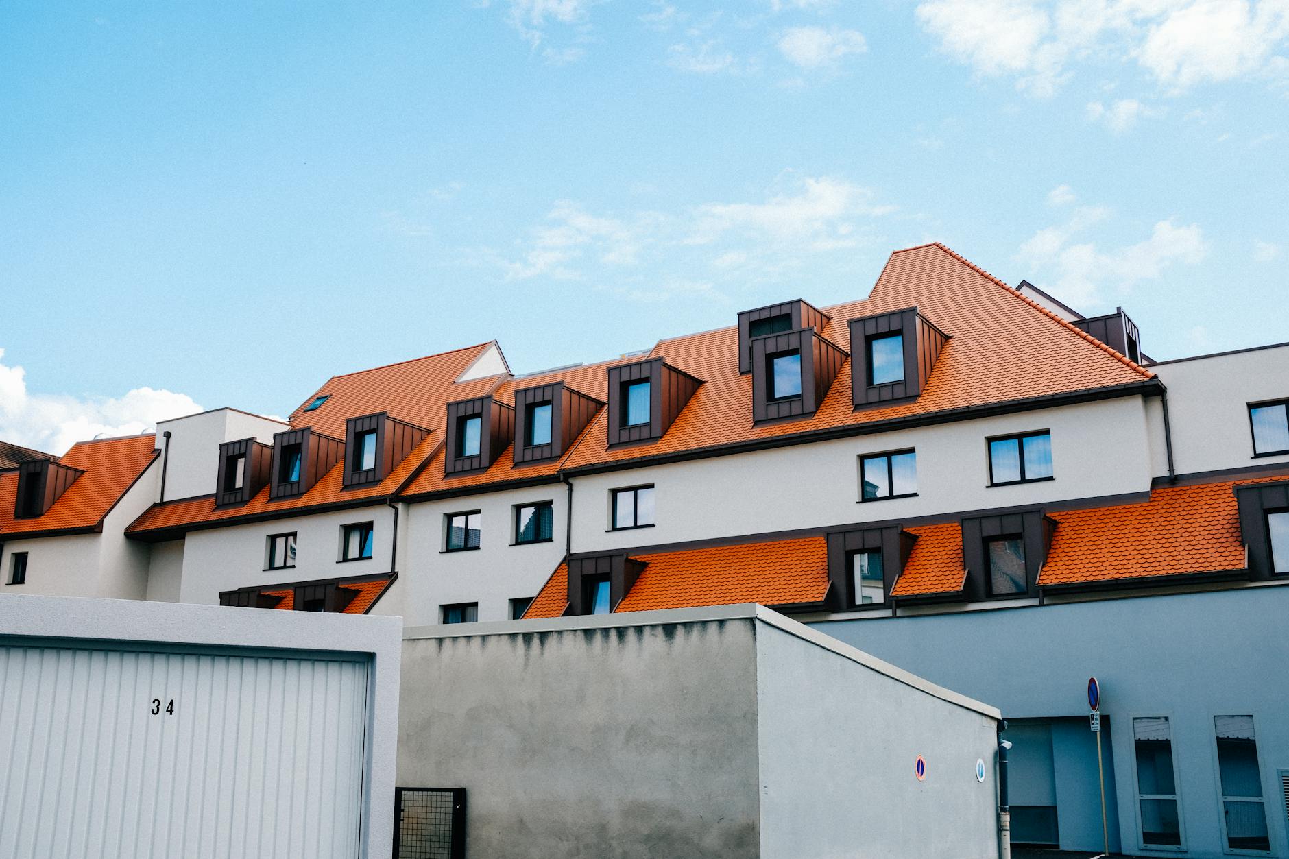 Ocieplenie dachu pianką PUR a wentylacja poddasza: jak uniknąć kondensacji pary Nowoczesny dom z pomarańczowym dachem na tle błękitnego nieba