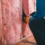 Pracownik w rękawicach montuje różową wełnę mineralną jako ocieplenie