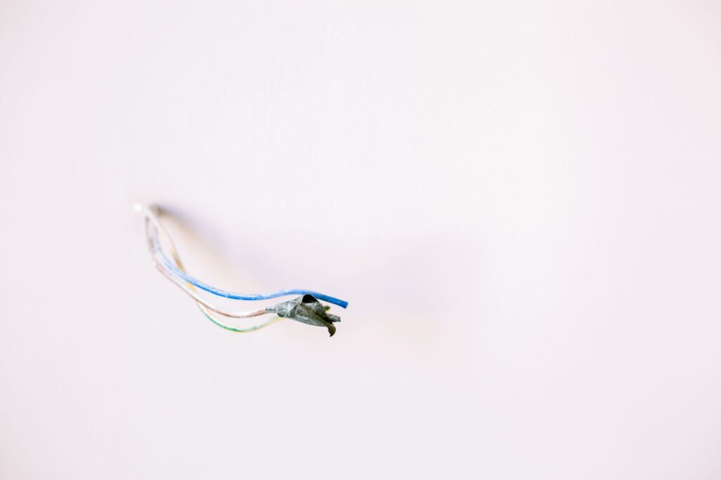 Luźne przewody elektryczne wystające z białej ściany